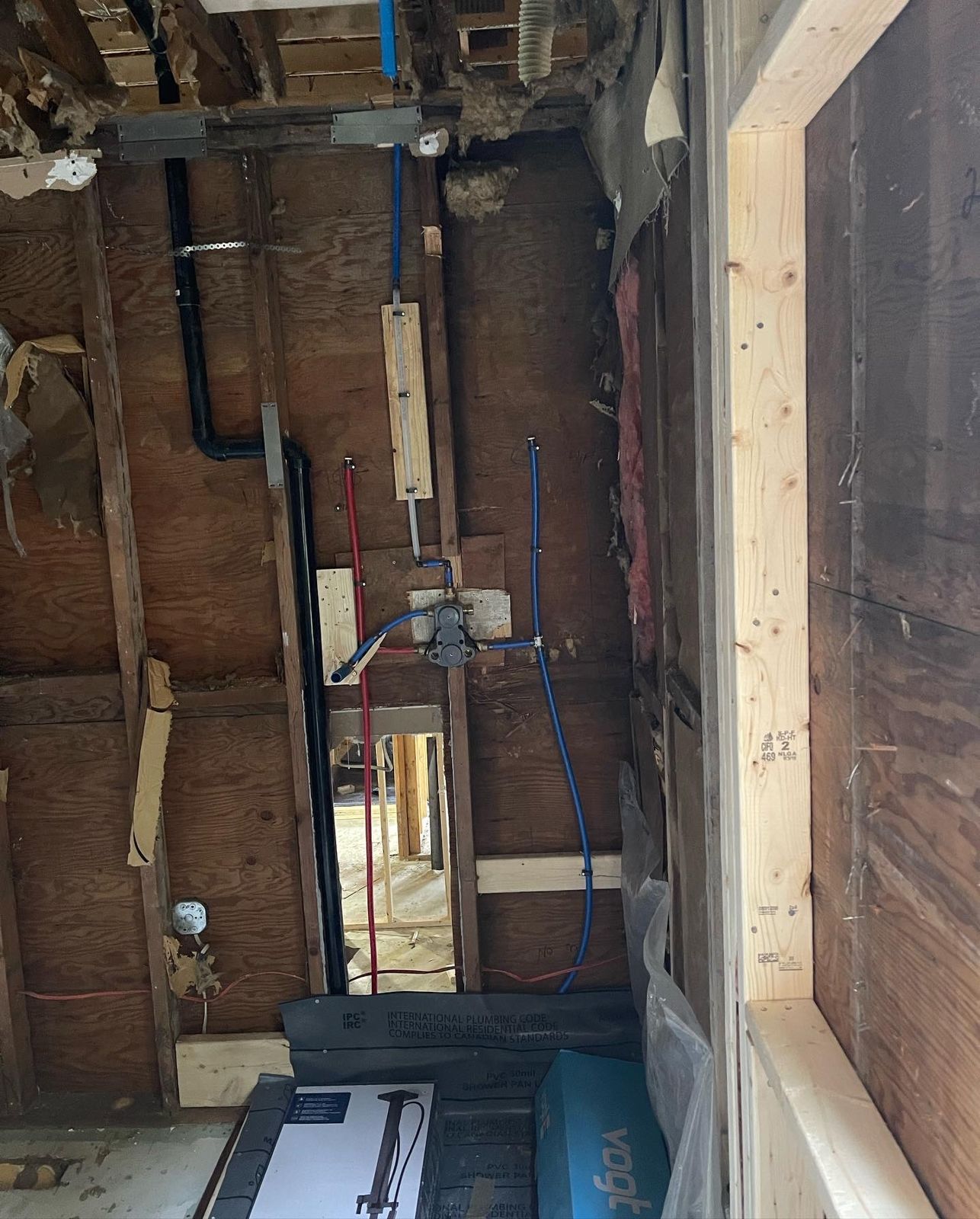 Opened bathroom wall with new black drain stack, PEX lines and shower valve
