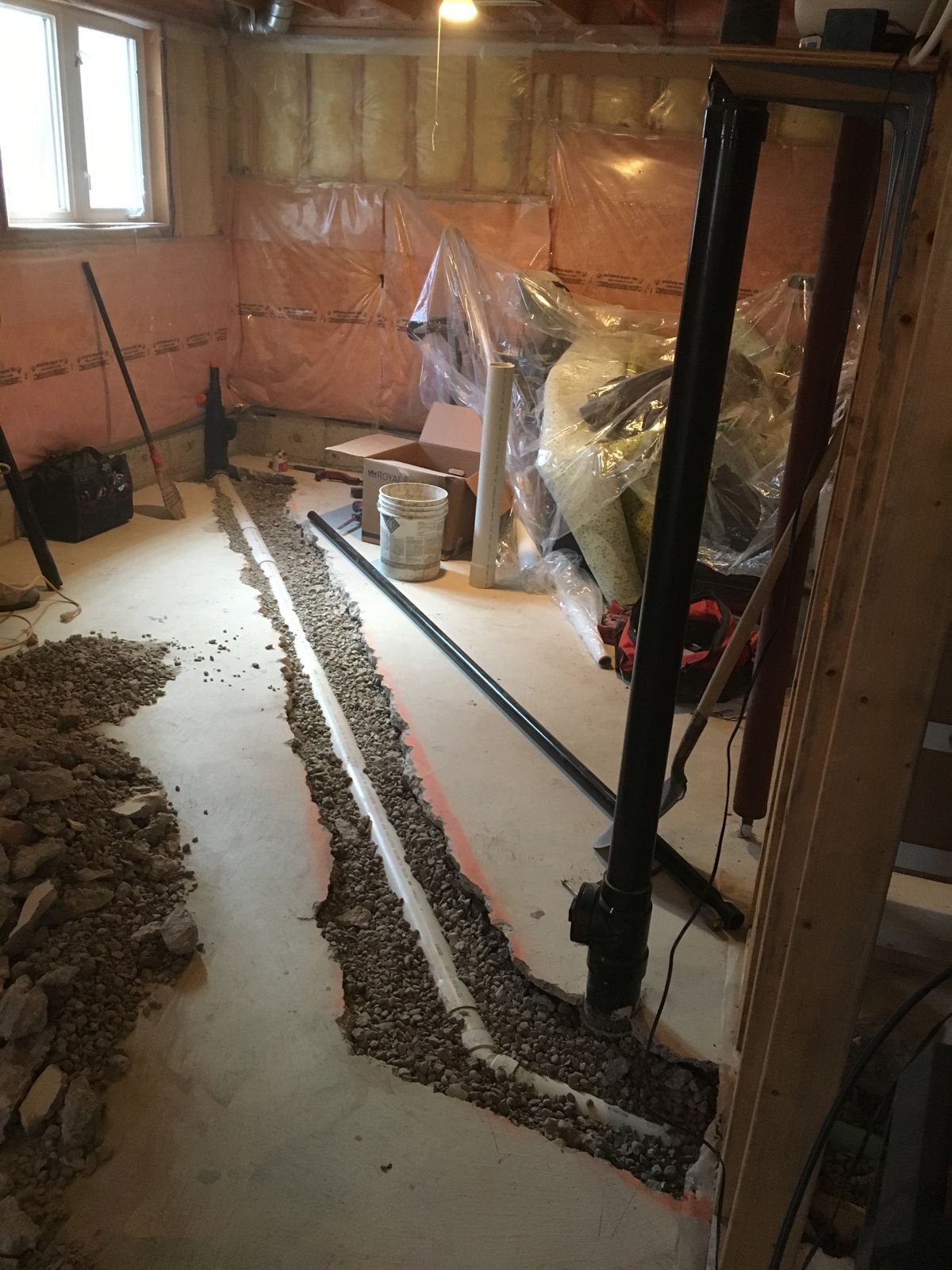 White drain pipe laid in a gravel trench cut through a basement floor