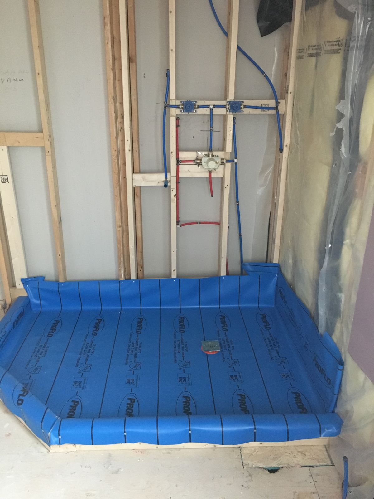 Shower valves roughed in with PEX above a blue PVC shower pan liner
