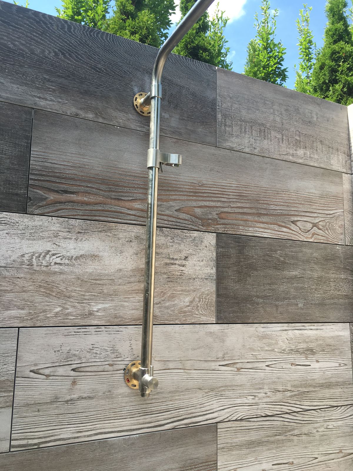 Stainless outdoor shower column mounted on a wood-look tile wall