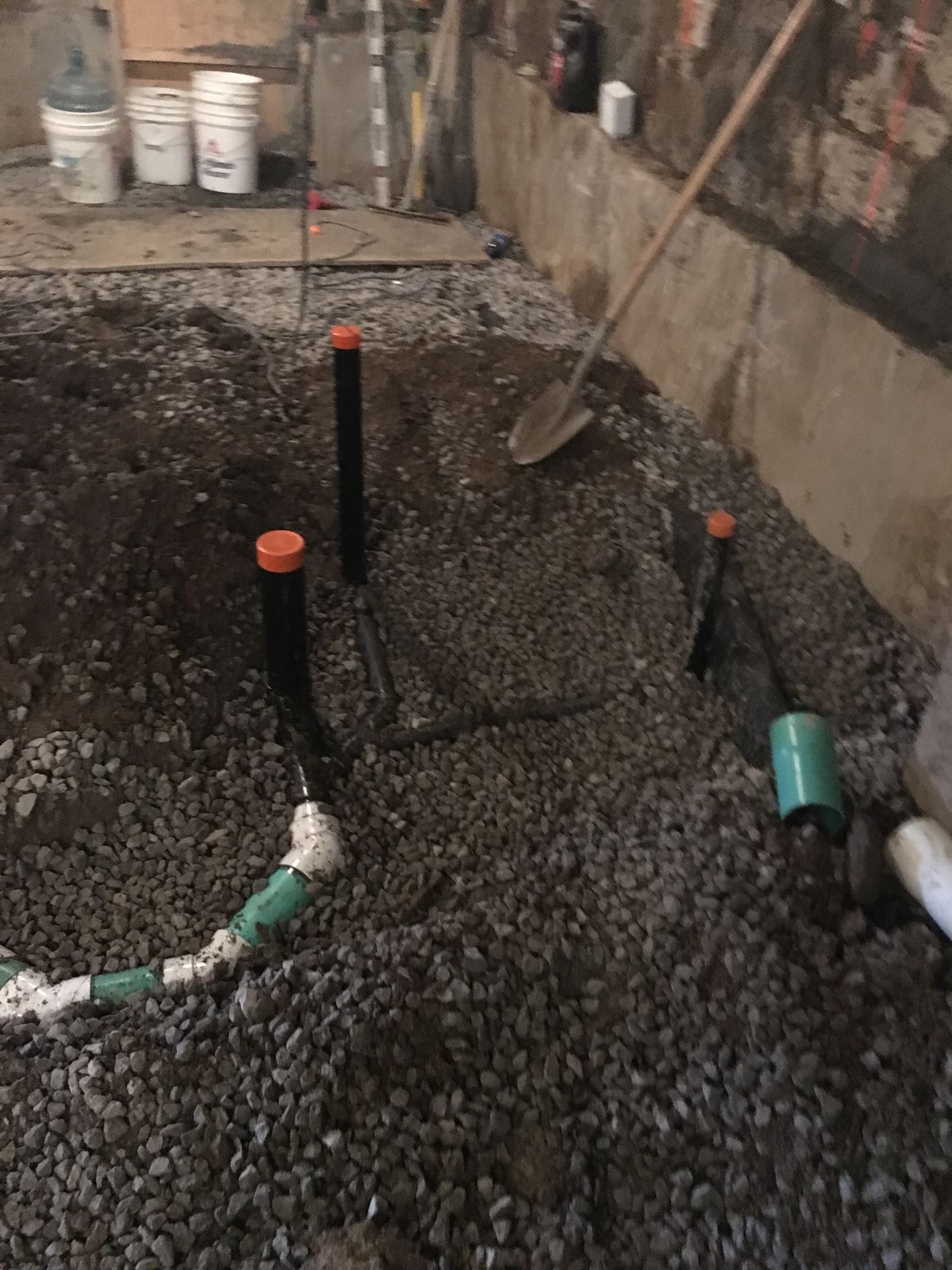 Capped drain stubs rising from gravel in a basement excavation