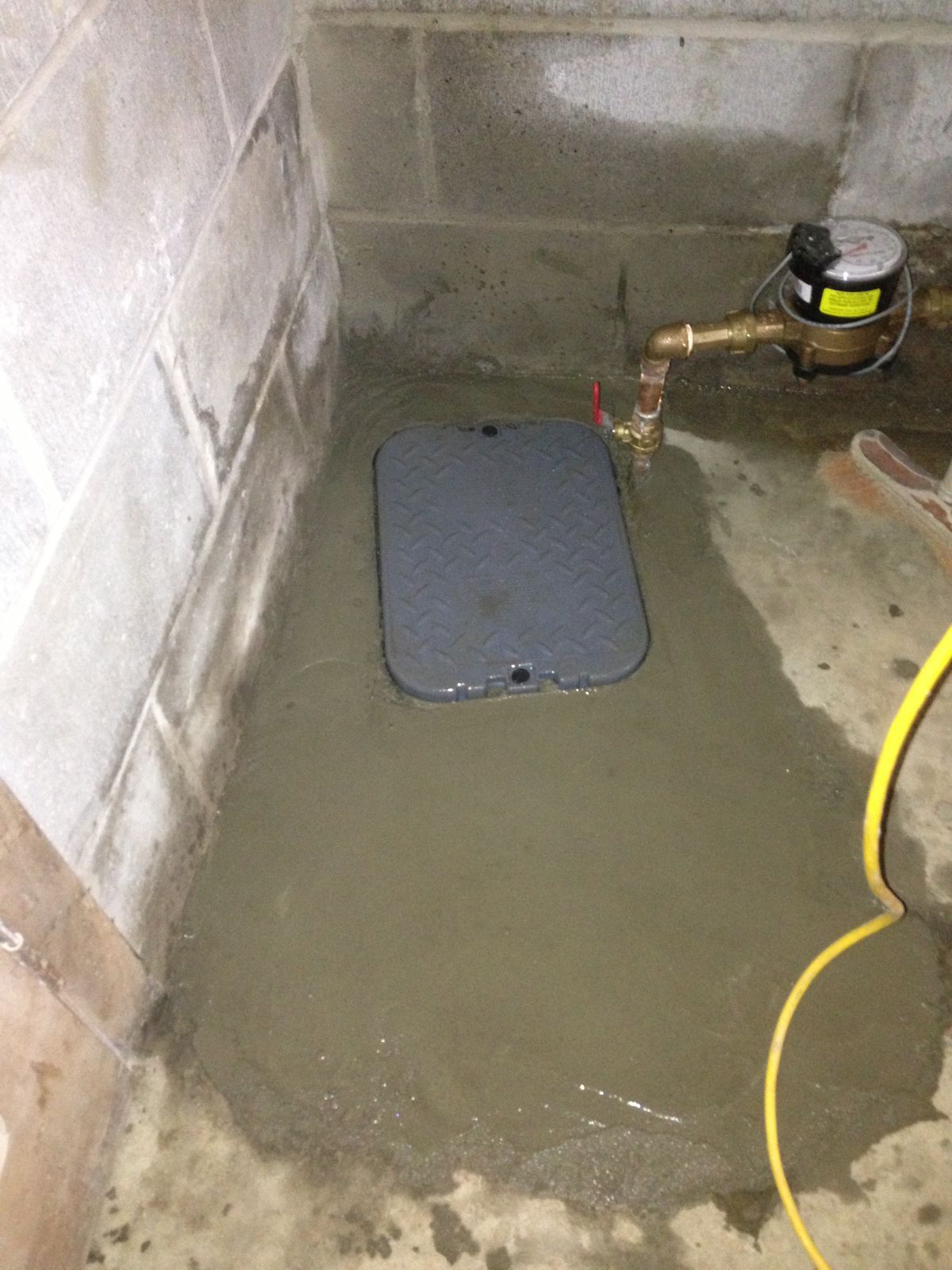 Grey access cover set in new concrete next to a water meter