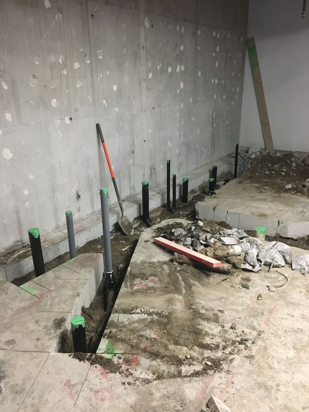 Row of capped drain pipes along a basement wall with the slab cut open